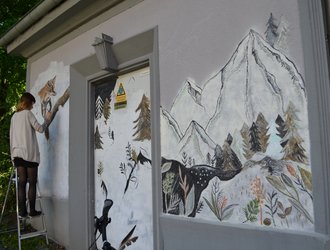 Frau auf Leiter malt Schneeberge und Fuchs auf Stawag Trafostation