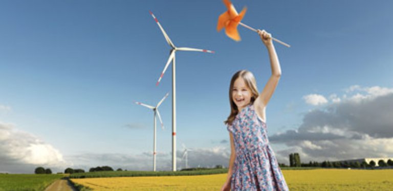 Mädchen auf Feld mit Energiewindräder hält Spielzeugwindrad in der Hand