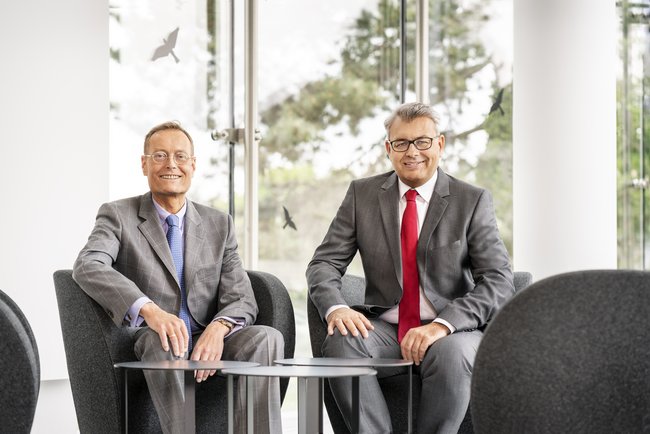 Dr Becker und Wilfried Ullrich sitzen gemeinsam am Tisch und lächeln
