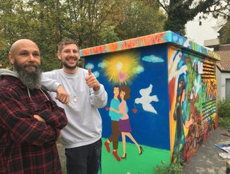 Zwei Männer stehend vor bunt besprühter STAWAG Trafostation in Aachen, Street Art Station Gangolfsweg 