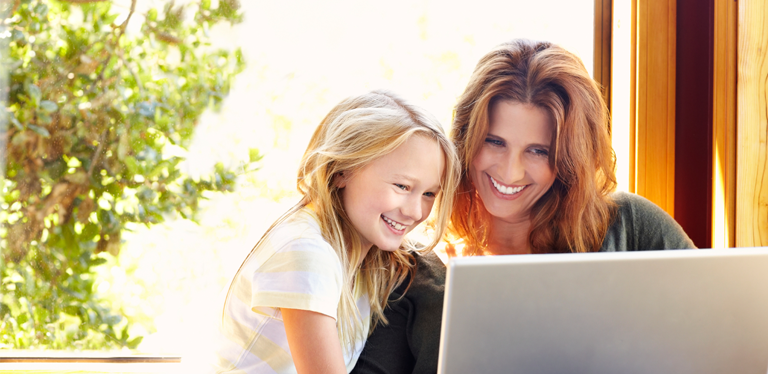 Mutter und Tochter schauen lächelnd auf Laptop-Bildschirm