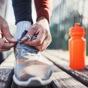 Person bindet sich Sportschuh auf Holzbank, daneben steht orangene Trinkflasche