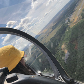Fotoaufnahme aus einem Segelflugzeug heraus, auf der linken Hälfte im Anschnitt Fenster und Person