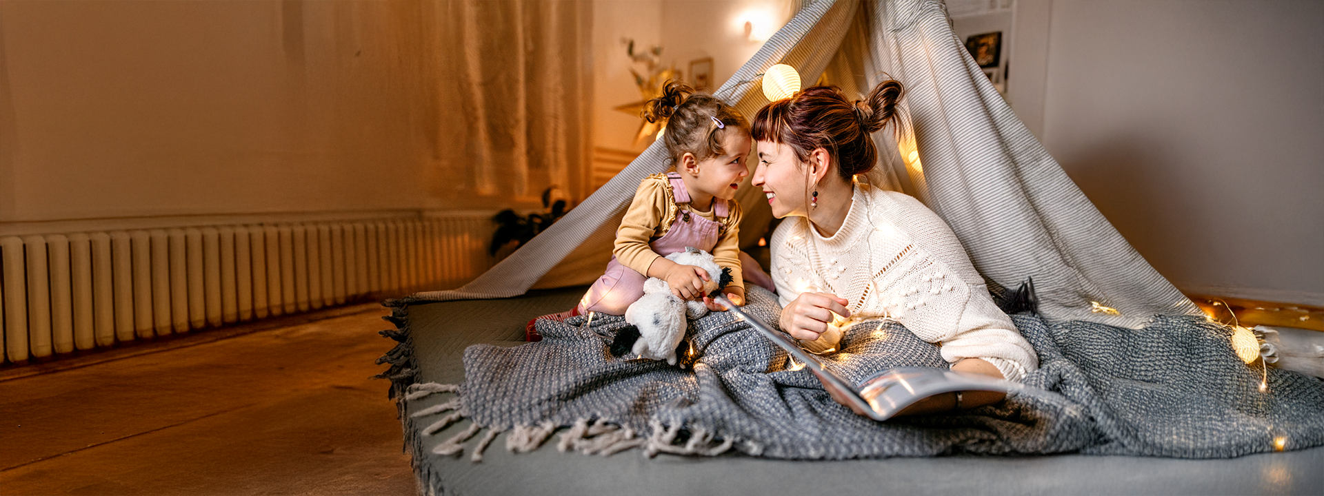 Frau sitzt mit Kind auf Decke in Tipi auf Wohnzimmerboden